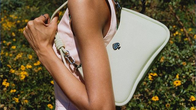 Two people holding Kate Spade handbags outdoors in a field with yellow flowers.