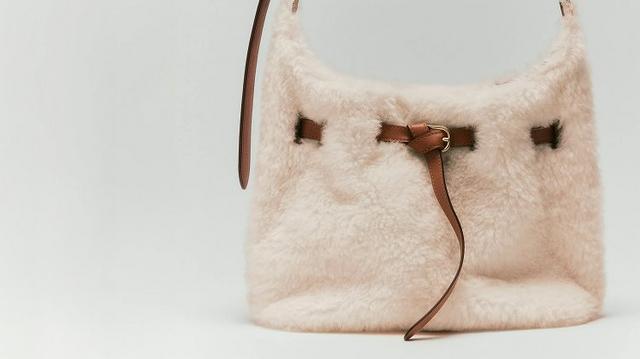 Cream-colored fuzzy bucket bag with brown leather drawstring closure and shoulder strap.