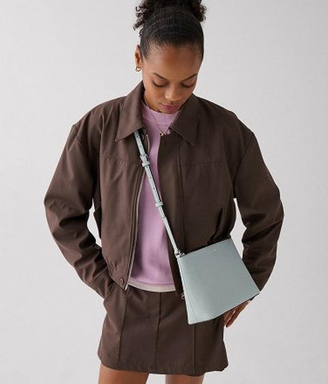 Woman wearing brown zip-up jacket, purple shirt, and brown shorts with mint green crossbody bag.
