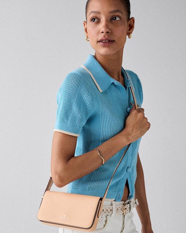 Woman wearing blue knit polo shirt with white trim, carrying a beige crossbody bag and gold jewelry.