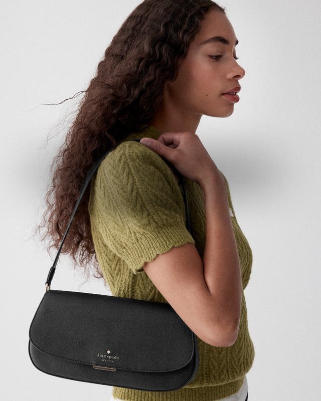 Woman wearing olive green short-sleeve sweater carrying a black kate spade new york shoulder bag.
