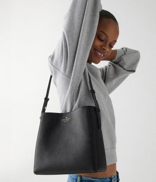 Woman wearing gray hoodie with kate spade black leather crossbody bag and smiling.