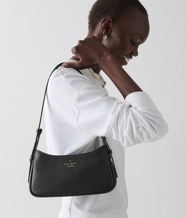 Model wearing a white long-sleeve top with pearl necklace, carrying a black Kate Spade shoulder bag.