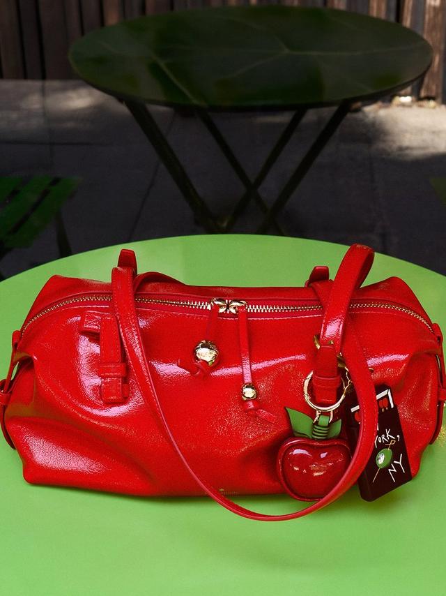 Red leather handbag with gold hardware and heart-shaped charm on green surface.