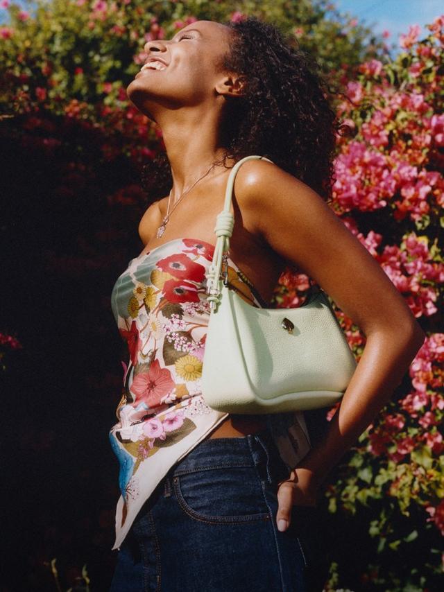 Person wearing a floral print dress carrying a mint green shoulder bag with decorative strap.