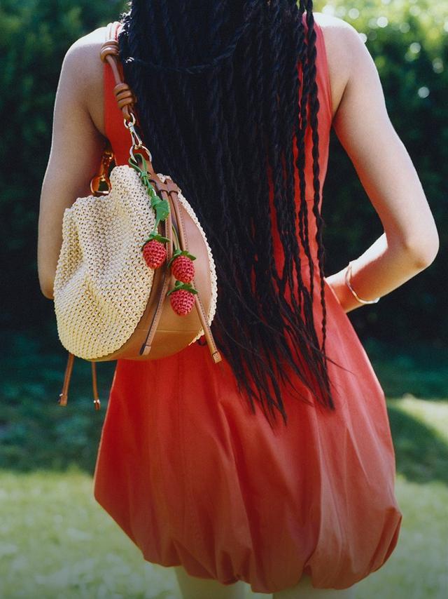 Person carrying beaded cream handbag with decorative strawberry charms attached to the strap.
