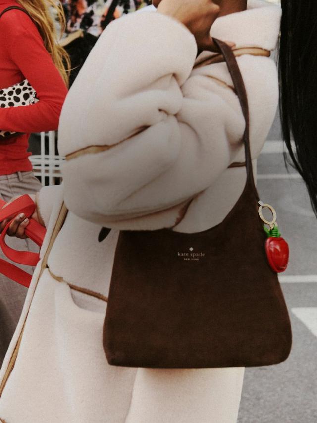 Person walking a dalmatian while carrying a brown kate spade new york handbag with strawberry charm.
