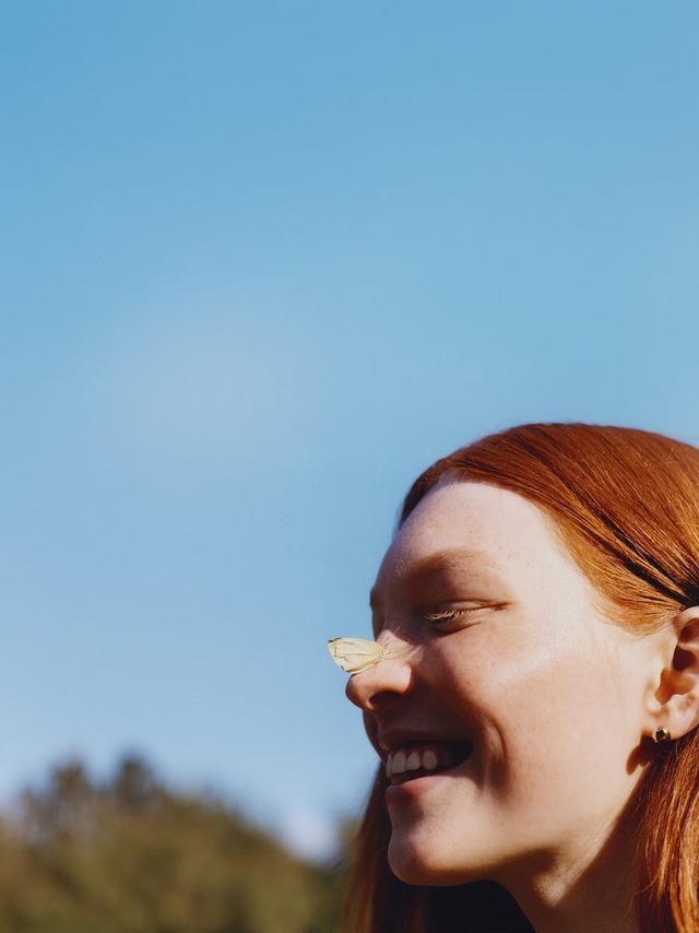 a woman with red hair smiling with a butterfly on her nose
