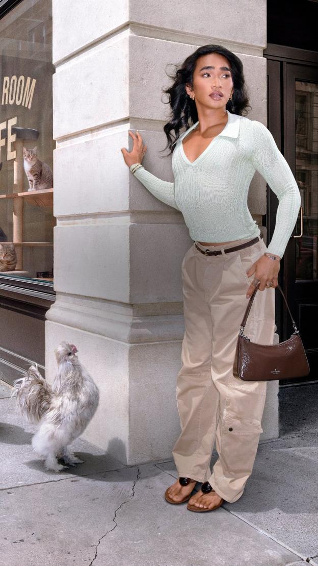 Woman in white cardigan and beige pants reacting to chickens on urban sidewalk near cat cafe.